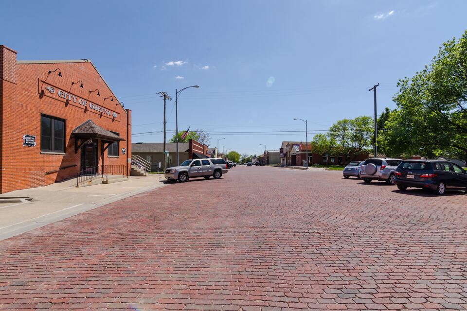 Red brick-paved street with brick commercial buildings and parked cars in downtown Gretna.