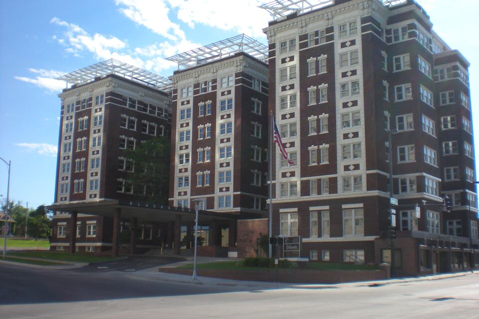 Tall historic brick and stone apartment building on a street corner under a partly cloudy sky.