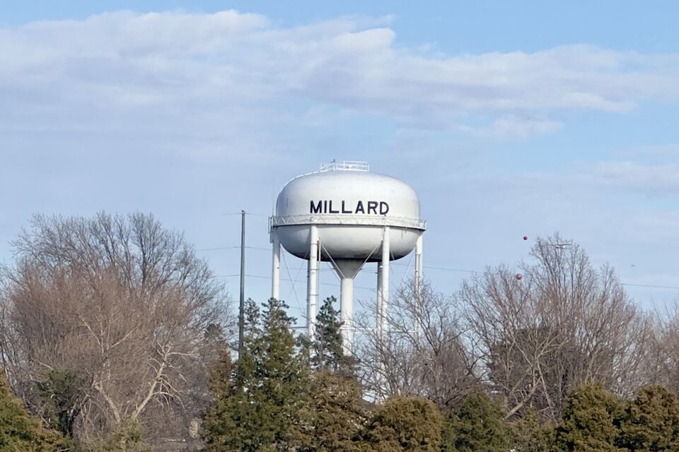 White water tower labeled Millard rising above bare winter trees under a blue sky.